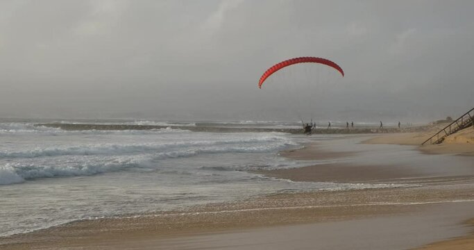 Pilot Man flying a Powered Paragliding PPG motor parachute. Flying with a sense of freedom, beautiful sunset nation day, Portugal ocean empty beach. Air extreme sports in slow motion, low above ground