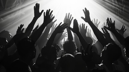 A crowd of people with their hands raised in the air, with a bright light shining down on them.