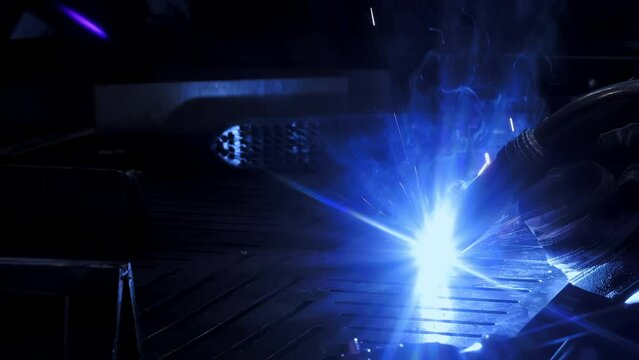 Factory worker welds metal. The man is welding. Welding with argon or electrode, using a welding machine. An industrial enterprise producing metal structures. Sparks and flashes fly. 