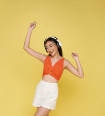 Happy young asian woman listening music with headphone dancing isolated on yellow background. People lifestyle relax concept.