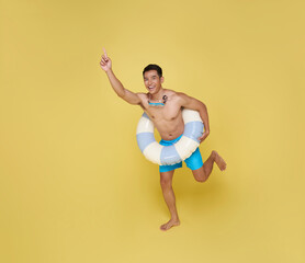 Full body young tourist asian man holding inflatable ring jumping happy summer vacation beach party isolated on yellow background.
