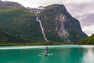 Man swims on a SUP board on the water in the Norwegian fjords. Landscape of Norway. Young male...