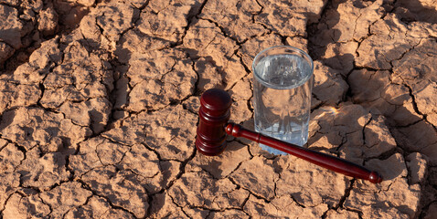 A glass of clean water and a judge's gavel on heat-cracked clay in the desert