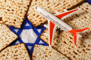 Small toy airplane resting on matzah pieces that are arranged around a blue and white Star of David. The airplane with orange wings and a white body is detailed. The matzah showcases its baked texture