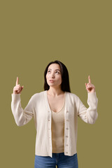 Asian woman in cardigan pointing up isolated on green 