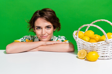 Photo of cute attractive lady folded arms over table basket lemon slices make fresh juice in summer isolated over green color background - obrazy, fototapety, plakaty