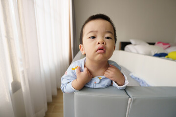 Pajamas Asian baby boy standing and scratching neck skin after waking up