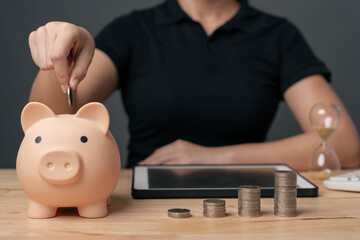 Young businesswoman is inserting coins into a piggy bank. Concept of savings and financial...