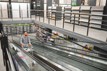 A man with a shopping cart on an escalator in a hardware store.