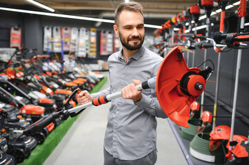 happy customer with electric lawn trimmer in hands at garden equipment store