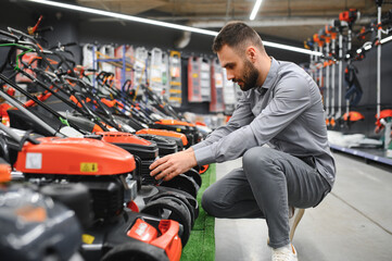 Young man buys a new lawnmower in a garden supplies store