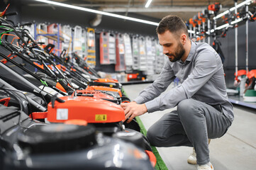 a customer examines new models of lawn mowers in an electrical store for gardeners and...