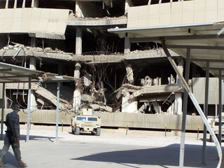 Military vehicles parked in front of a bombed out building at FOB Loyalty during Operation Iraqi...