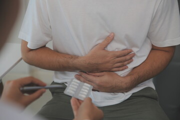Man suffering with severe stomach pain sitting at home. Hand of mature guy holding abdomen...