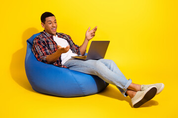 Full length photo of attractive guy wear checkered shirt sitting on bean bag talk on laptop webcam...