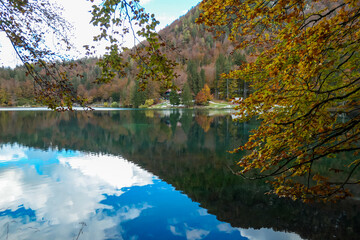 Fototapeta na wymiar Panoramic view of Fusine Lake (Laghi di Fusine) in Tarvisio, Friuli-Venezia Giulia, Italy, Europe. Water reflection in clear green alpine lake. Autumn colored foliage. Calm serene tranquil atmosphere