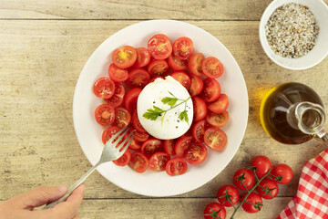 Fresh cherry tomatoes salad with burrata and olive oil on a plate on wooden background. Top view. Summer food concept