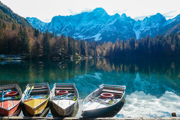 Colorful wooden boats on Fusine Lake (Laghi di Fusine) with scenic view of snow capped Julian...