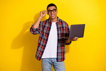 Portrait of nice young man touch glasses hold laptop wear shirt isolated on yellow color background