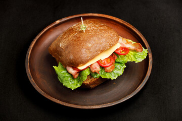 Sandwich with cheese, tomatoes, lettuce and bacon on black bread