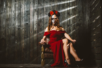 A captivating woman dressed in red with traditional Day of the Dead makeup sits confidently, her...