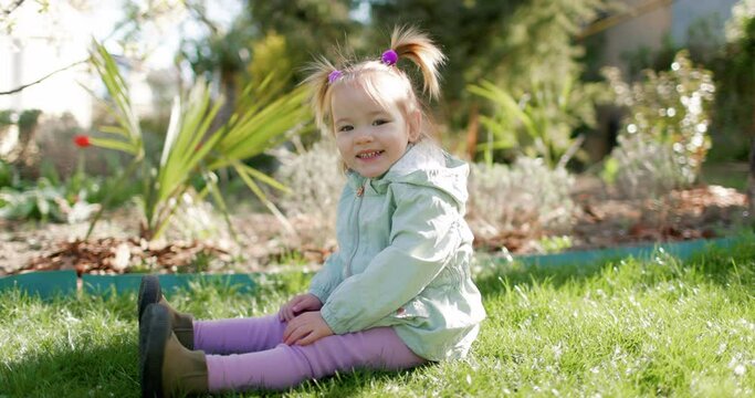 Beauty cute child girl in spring garden sitting on lawn. Smiling baby girl