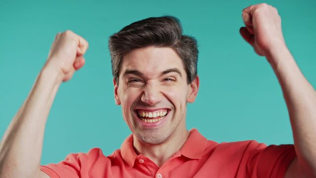 Handsome man on blue shows triumph yes YEAH gesture of victory, achieved results