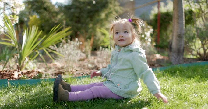 Happy cute child girl in spring garden sitting on lawn. Pretty little daughter
