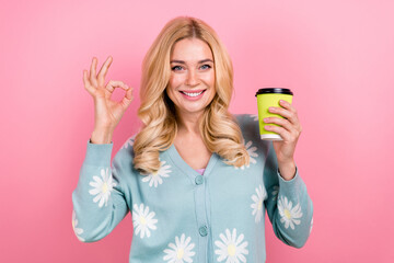 Photo of satisfied woman with wavy hairdo dressed print cardigan hold cup of cappuccino show okey...