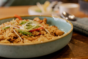 Close up of fried rice with chicken and vegetables served on a blue ceramic plate on wooden table. Asian cuisine, stir fry rice. Copy space