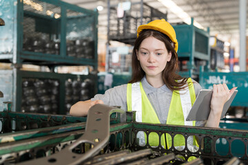 Female warehouse worker wearing safety uniform working with digital tablet and inspecting quality for auto spare parts at warehouse