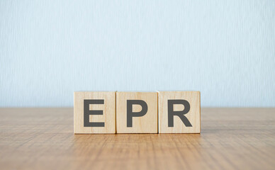 Wooden blocks spelling EPR on a wooden surface against a textured blue wall