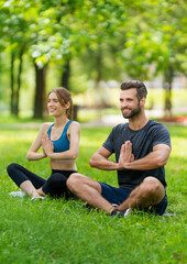 Full body young couple  sitting in lotus position or woman practicing with man, brunette bearded coach trainer, doing yoga exercises or meditating together, after outside training.