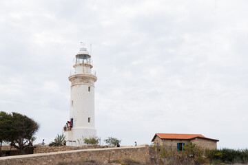 Fototapeta na wymiar White lighthouse and small house cloudy sky as a background