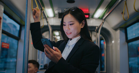 Asian woman in formal clothing standing still in middle of bus or train. Holding steel pole for...