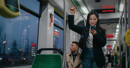 Camera view of young Asian woman hand holding handle on public train or bus. Busy passenger texting...