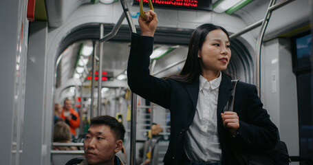 Camera view of Asian young woman in formal clothes holding handrail in urban train or bus. Pretty...