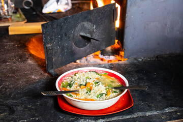 Teller mit Nudelsuppe und Gemüse neben einem Ofen in einer Lodge in Nepal - 793085828