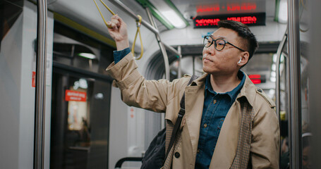 Handsome Chinese male commuting back home after difficult working day. Waiting for his stop....