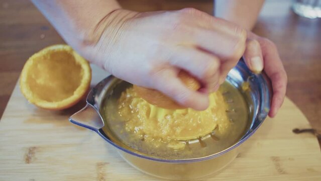 Close up of woman's hands pressing, squeezing orange juice using manual juicer. Female cook, chef preparing orange juice in a brightly lit kitchen. Studio shot. High quality 4k footage