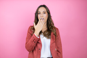 Young beautiful woman wearing casual jacket over isolated pink background covering mouth with hand,...