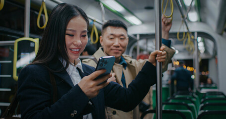 Asian girl standing in middle of large wagon of train or metro. Watching videos or images on...