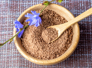 Ground chicory root on a wooden spoon and chicory flowers on a rustic wooden background. Alternative medicine. Healthy drinks. chicory drink - obrazy, fototapety, plakaty