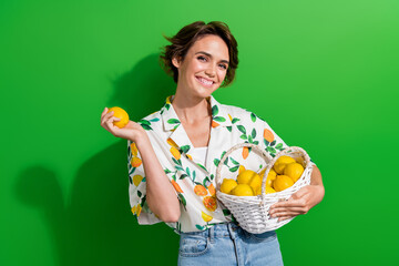 Photo of optimistic young lady bob brown hair hold basket many citrus fruits summer grocery market isolated on green color background - obrazy, fototapety, plakaty