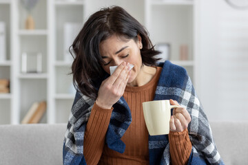 Young woman sick at home, blowing nose and holding a mug