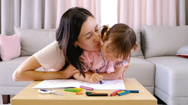 Mom kisses a child todler who draws with colored pencils