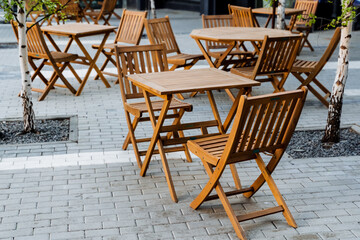 Fototapeta na wymiar Outdoor furniture set with wooden folding tables and chairs on a brick sidewalk