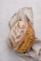 Artisan sourdough homemade loaf of bread on linen napkin, concrete background. Natural light with soft shadows, closeup view, copy space
