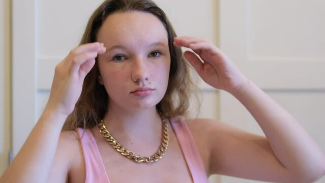 Sad young girl straightens her hair on her neck gold chain pink dress teenager young woman