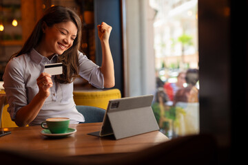 Happy woman holding credit card in coffee shop. Successful buying online